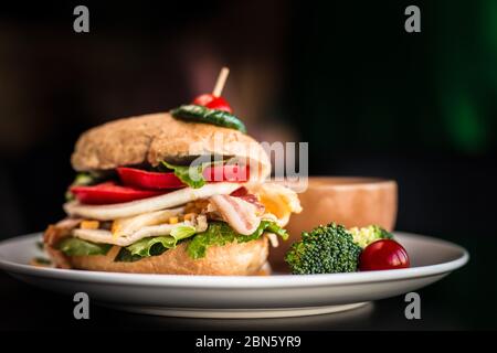 Nahaufnahme des geladenen Burger mit Kirschtomate Zahnstocher auf der Oberseite. Gemüse Speck Sandwich mit schwarzem Hintergrund. Stockfoto