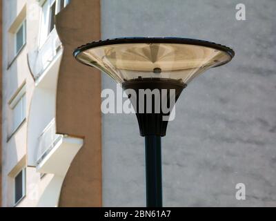 Moderne Straßenbeleuchtung mit kreisförmigem Design und klare Glaslinse auf der Oberseite des Aluminium-Lichtmastes. Verschwommenes Apartmentgebäude Beton außen und Balkone Stockfoto