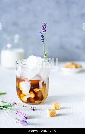 Glas Kaffee mit Eis, Milch und Lavendelblüten auf einem hellen Hintergrund. Kaltes Sommergetränk. Stockfoto