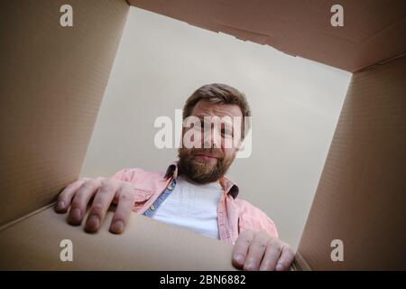 Der Mensch schaut in eine ausgepackte, gelieferte Schachtel und ist verärgert, weil er die falsche Bestellung erhalten hat. Auspacken von innen. Stockfoto