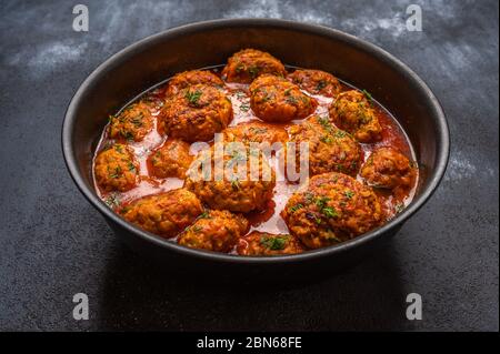 Hausgemachte Fleischbällchen in Tomatensauce mit Kräutern in einem Topf auf dunklem Holzhintergrund Stockfoto