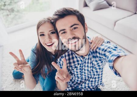 Fröhliche, verspielte Schwester und Bruder machen Selfie und zeigen Friedenszeichen. Sie sind zuhause, in lässigen Outfits. Beide haben Strahlungsstrahlen Stockfoto