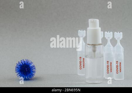 Abstraktes Modell des Coronavirus, Ampulle mit Medizin und Flasche mit antibakteriellem Gel für Hände auf grauem Hintergrund. Die Ampulle sagt Covid-19. Pandemierisiko Stockfoto