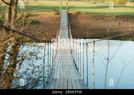 Alte hängende hölzerne Fußbrücke über den Fluss. Foto an einem Sommertag. Flussüberquerung für Menschen Stockfoto