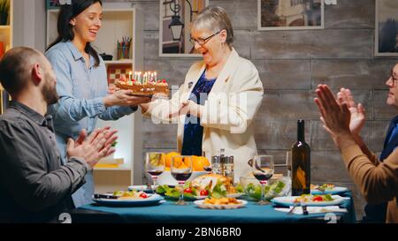 Ältere Frau feiert ihren Geburtstag mit der Familie. Leckerer Kuchen bei Treffen mit Freunden und Familie. Zeitlupe aufgenommen Stockfoto