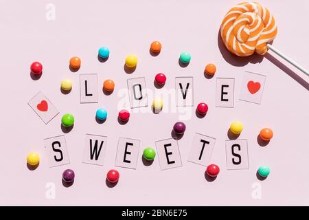 Sortiment von süßen Bonbons auf rosa Hintergrund.Bunte Bonbons und Text lieben Süßigkeiten.Flat Lay Zusammensetzung mit Gelee-Bohnen. Bunte Schokolade Bonbons Stockfoto