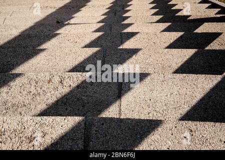 Abstrakter Hintergrund mit einem Muster, das von harten Schatten auf einer Betontreppe in der Stadt geschaffen wurde. Gesehen in Deutschland im Mai.