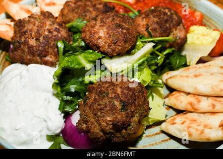 Mediterrane Fleischbällchen mit Salat, Kichererbsen mit Tomatensauce, Joghurt-Dip und Pita-Brot werden in einem Restaurant serviert, das einen Holztisch im Hintergrund darstellt. Stockfoto