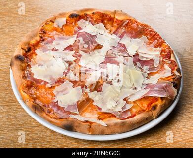 Italienische Pizza Ofen gebacken traditionell mit Tomatensauce, Mozzarella, Prosciutto, Rucola, Parmesan Späne. Einfache braune hölzerne Restaurant Tisch-Setti Stockfoto