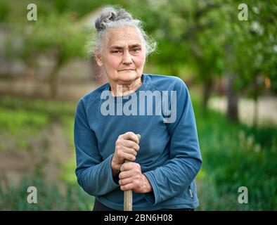 Alte Bäuerin mit Hacke in ihrem Garten Stockfoto