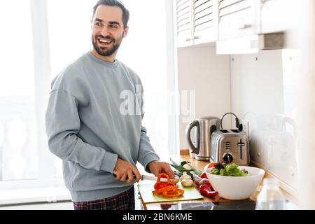 Bild von zufrieden gutaussehenden Mann in Casual Wear lächelnd und Mittagessen in hellen modernen Küche Stockfoto