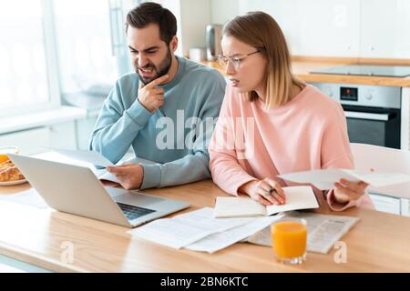 Porträt von jungen irritierten Paar Arbeit mit Laptop und Dokumente in der gemütlichen Küche zu Hause Stockfoto