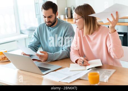 Porträt von jungen irritierten Paar Arbeit mit Laptop und Dokumente in der gemütlichen Küche zu Hause Stockfoto