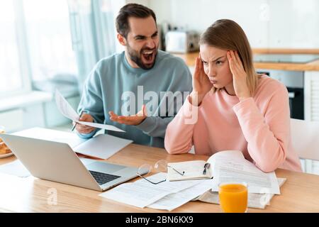 Porträt von jungen verärgerten Paar Streit während der Arbeit mit Laptop und Dokumente in der Küche zu Hause Stockfoto
