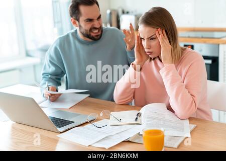 Porträt von jungen verärgerten Paar Streit während der Arbeit mit Laptop und Dokumente in der Küche zu Hause Stockfoto
