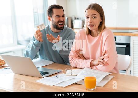 Porträt von jungen verärgerten Paar Streit, während der Hand Kreditkarte und Laptop in der Küche zu Hause Stockfoto