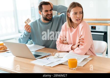 Porträt von jungen verärgerten Paar Streit, während der Hand Kreditkarte und Laptop in der Küche zu Hause Stockfoto
