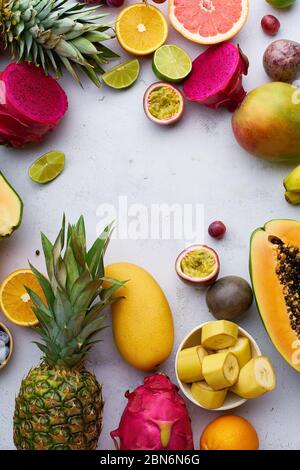 Tropische Früchte flach legen mit Mango, Papaya, Pitahaya, Passionsfrucht, Trauben, Limetten und Ananas. Tisch mit Zutaten für Sommernaschen auf concre Stockfoto