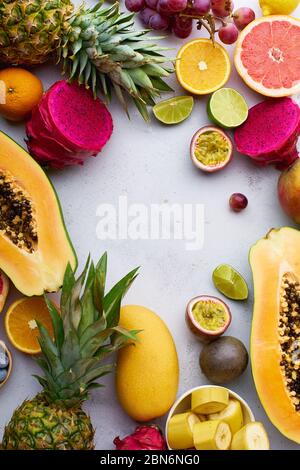 Tropische Früchte flach legen mit Mango, Papaya, Pitahaya, Passionsfrucht, Trauben, Limetten und Ananas. Tisch mit Zutaten für Sommernaschen auf concre Stockfoto