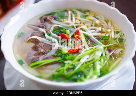 Asiatische Lebensmittel.Vietnamesische Pho bo Suppe mit Rindfleisch, Reisnudeln in Brühe und Gewürze in weißen Schüssel serviert.traditionelle vietnamesische Küche in close up.Delicio Stockfoto