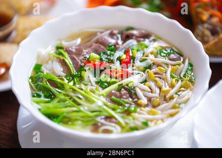 Vietnamesische Pho bo Suppe mit rotem Paprika und Gewürz mit gekochtem Rindfleisch, Sprotte Bohnen gemischt.Delicious Pho Brühe in weißen Schüssel auf dem Tisch in t serviert Stockfoto