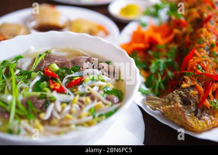 Pho bo Suppe & gebratenen Fisch im Veitnamesisch Restaurant.exotische Vietnam Küche auf dem Tisch serviert.köstliche asiatische Meeresfrüchte mit natürlichen Zutaten gekocht.Hot A Stockfoto