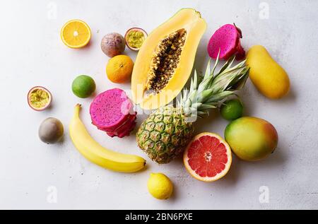 Tropische Früchte flach legen mit Mango, Papaya, Pitahaya, Passionsfrucht, Trauben, Limetten und Ananas. Tisch mit Zutaten für Sommernaschen auf concre Stockfoto