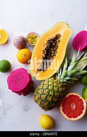 Tropische Früchte flach legen mit Mango, Papaya, Pitahaya, Passionsfrucht, Trauben, Limetten und Ananas. Tisch mit Zutaten für Sommernaschen auf concre Stockfoto