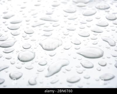 Transparente Wassertropfen auf einer weißen glänzenden Oberfläche. Abstrakter Hintergrund mit starker Unschärfe-Zone. Stockfoto