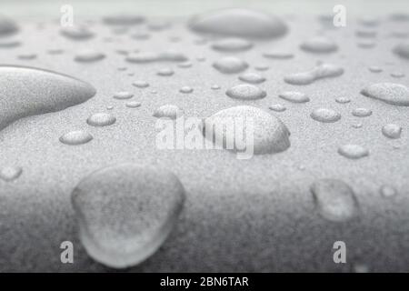 Transparente Wassertropfen auf einer silberglänzenden Metalloberfläche. Abstrakter Hintergrund mit starker Unschärfe-Zone. Stockfoto