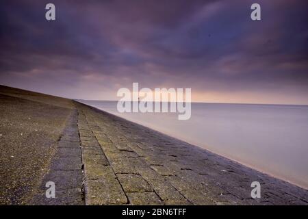 Beeindruckende Aussicht vom Deich bei Moddergat, Niederlande. Schöne Komposition aus Steinen, Wasser und Luft. Sonnenuntergang über dem Wattenmeer. UNESCO-Welt Stockfoto