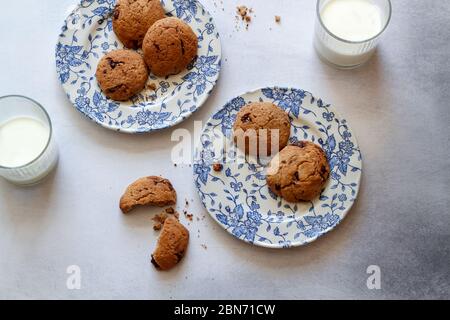 Chocolate Chip Cookies auf blauen Tellern und 2 Gläser Milch auf einem grauen Küchentisch Stockfoto