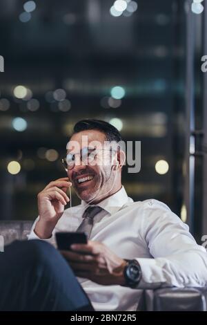 Lächelnder Geschäftsmann, der in der Flughafenlounge telefoniert. Mann, der am Flughafen auf seinen Flug wartet und mit dem Handy telefoniert. Stockfoto