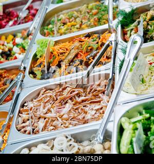 Salate, marinierte Champignons mit Zwiebelringen, Speck in Scheiben, geschmorte Auberginen mit Karotten, frische Gurken in gastronomischen Behältern mit Metalllöffel Stockfoto