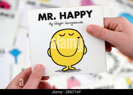Ein Junge, der das Buch Mr Men lesen möchte, Mr Happy von Roger Hargreaves Stockfoto