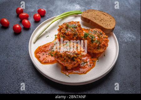 Hausgemachte Fleischbällchen in Tomatensauce auf einem weißen Keramikplatte mit Brot, Zwiebeln und Tomaten Stockfoto