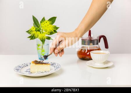 Hand halten Gabel Essen baskischen verbrannt Käsekuchen mit Tasse Tee auf dem Tisch. Stockfoto