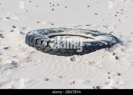 Großer schwarzer Gummireifen links auf einem Sandstrand, Umweltverschmutzung Konzept Stockfoto