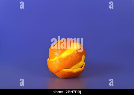 Orange mit geschälter Spiralhaut auf violett-blauem Hintergrund. Stockfoto