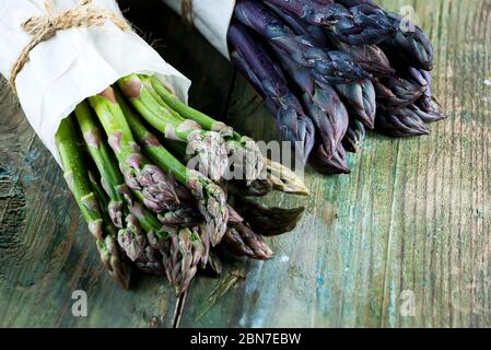 Zwei Bündel von hausgemachten rohen Bio-lila und grünen Spargel Speere zum Kochen gesunde vegetarische Ernährung Lebensmittel auf einem hölzernen Hintergrund, kopieren Raum Stockfoto