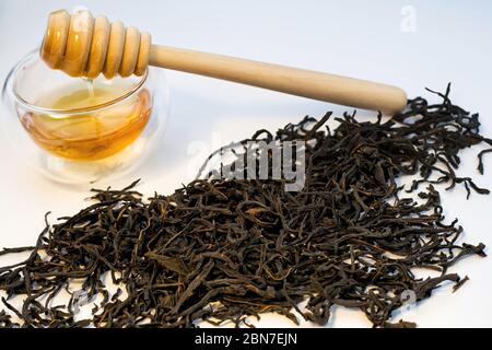 Trockene schwarze Teekräuter mit Honig auf weißem Hintergrund. Stockfoto