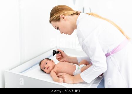 Der Kinderarzt untersucht das 2-wöchige Ohr des alten Babys in der neuen pädiatrischen Klinik. Junger Arzt, der Otoskop (Auriskop) verwendet, um den Gehörgang und die Trommelmembran zu überprüfen. Stockfoto