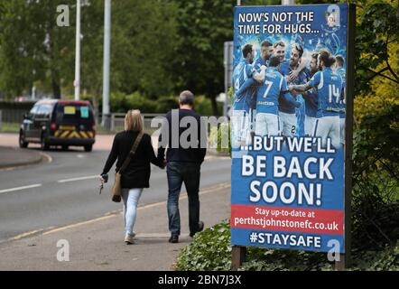 Die Leute gehen an einem Schild vorbei, das sagt: "Jetzt ist nicht die Zeit für Umarmungen ... aber wir werden bald wieder kommen!" Außerhalb des McDiarmid Park, dem Heimstadion von St Johnstone. Stockfoto