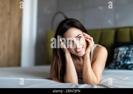 Die reine Schönheit. Schöne junge Frau ihr Haar einstellen und Suchen an der Kamera, während auf dem Bett zu Hause liegen Stockfoto