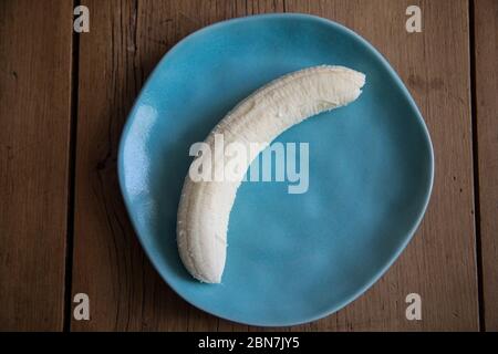 Geschälte Banane in einem blauen Teller auf einem Holztisch bereit zu essen Stockfoto