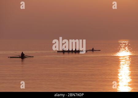 Ruderteam Training mit Trainer über dem schimmernden See bei Sonnenuntergang Stockfoto