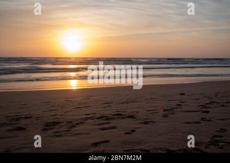 Goldener Sonnenuntergang über einem tropischen Strand und Meer, das sich auf dem Wasser spiegelt, mit sanften Wellen, die an der Küste brechen Stockfoto