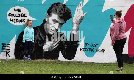 Lorna Mullins und ihre Tochter Penny Mullins (6) fotografieren mit der irischen Künstlerin Emmalene Blake das Wandbild von David Bowie in Süd-Dublin. Dies ist das jüngste in der Serie 'Stay at Home' des Dubliner Künstlers, der die Menschen dazu ermutigt, sich an soziale Distanzierungen zu halten. Andere Künstler waren Dua Lipa, Robyn und Cardi B. Stockfoto