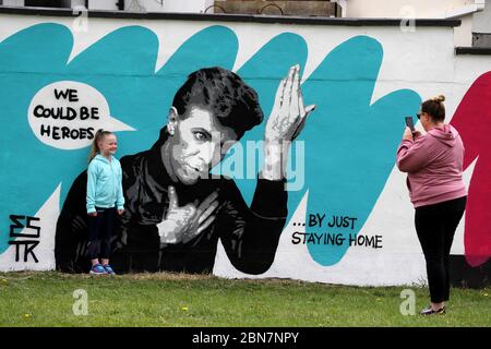 Lorna Mullins und ihre Tochter Penny Mullins (6) fotografieren mit der irischen Künstlerin Emmalene Blake das Wandbild von David Bowie in Süd-Dublin. Dies ist das jüngste in der Serie 'Stay at Home' des Dubliner Künstlers, der die Menschen dazu ermutigt, sich an soziale Distanzierungen zu halten. Andere Künstler waren Dua Lipa, Robyn und Cardi B. Stockfoto