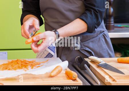 Mann schält Karotten und bereitet eine Mahlzeit auf einem Holzhackbretter Stockfoto